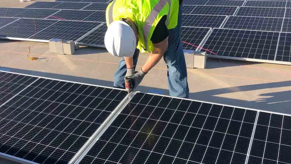 A crew member in a hard hat and hi-vis vest fastening solar panels into place