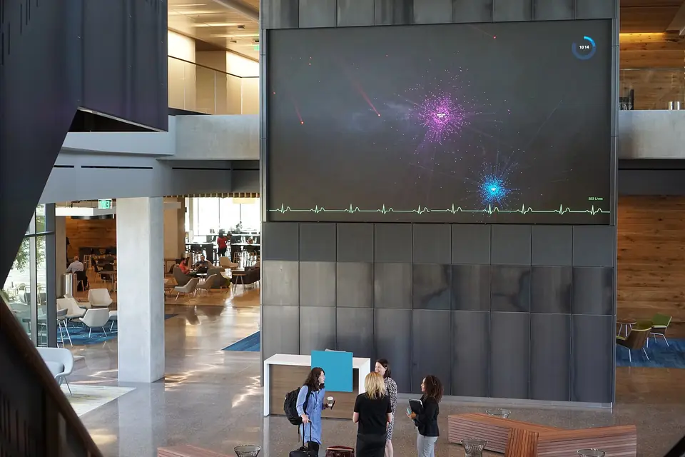 The lobby of a glass-and-concrete office building, where a wall-sized screen shows a heartbeat line under a glowing star field